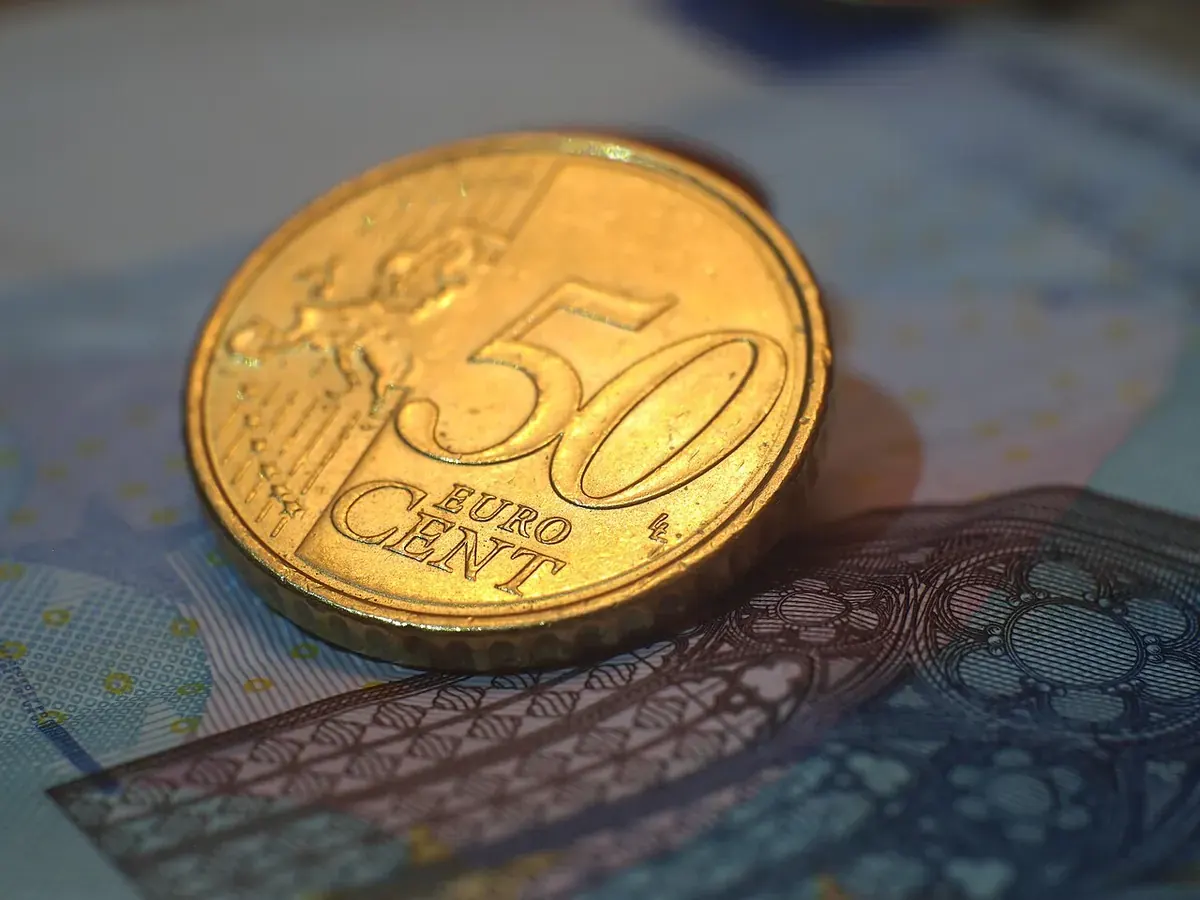 Едър план на монета от 50 евроцента, поставена върху синя банкнота от 20 евро